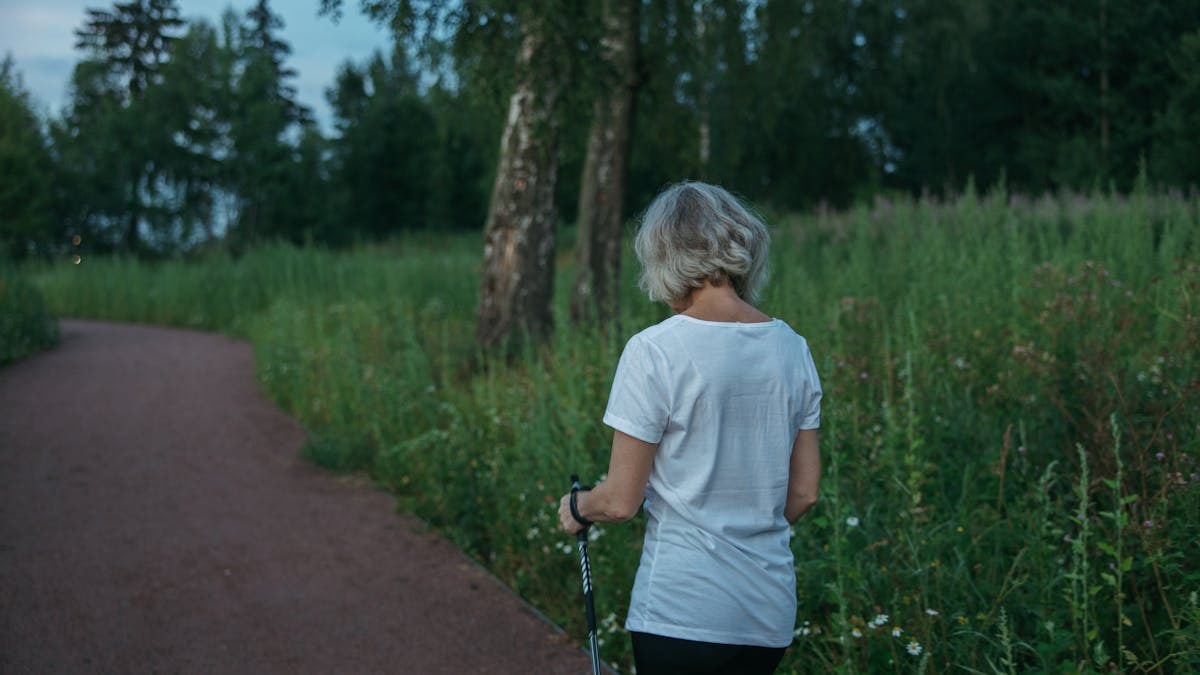 Elderly woman practicing Nordic walking on a park trail, promoting health and fitness.