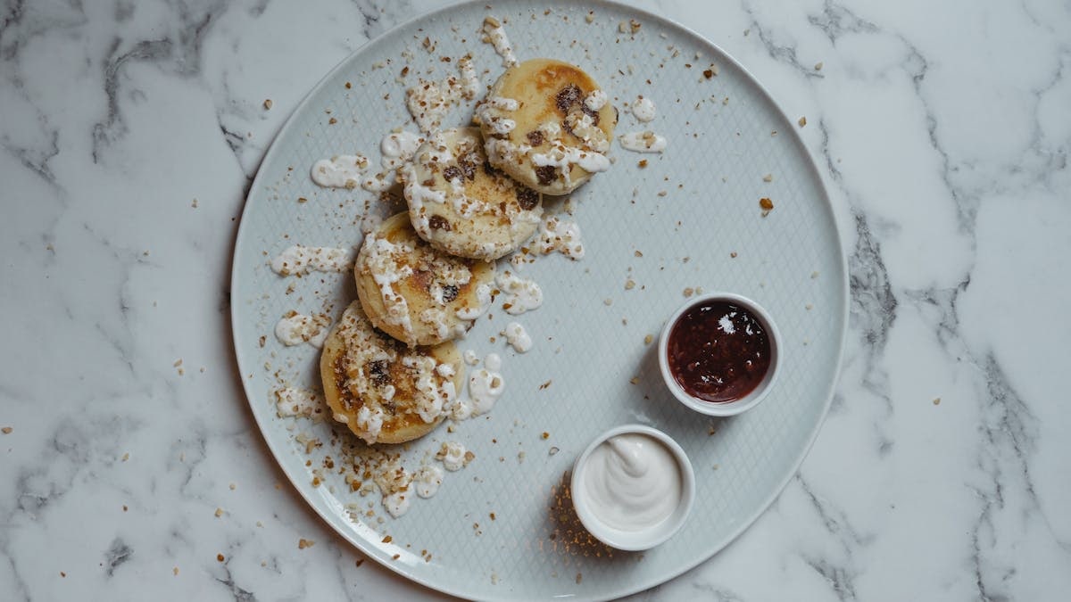 Overhead shot of pancakes topped with cream and paired with jam for a delicious breakfast.